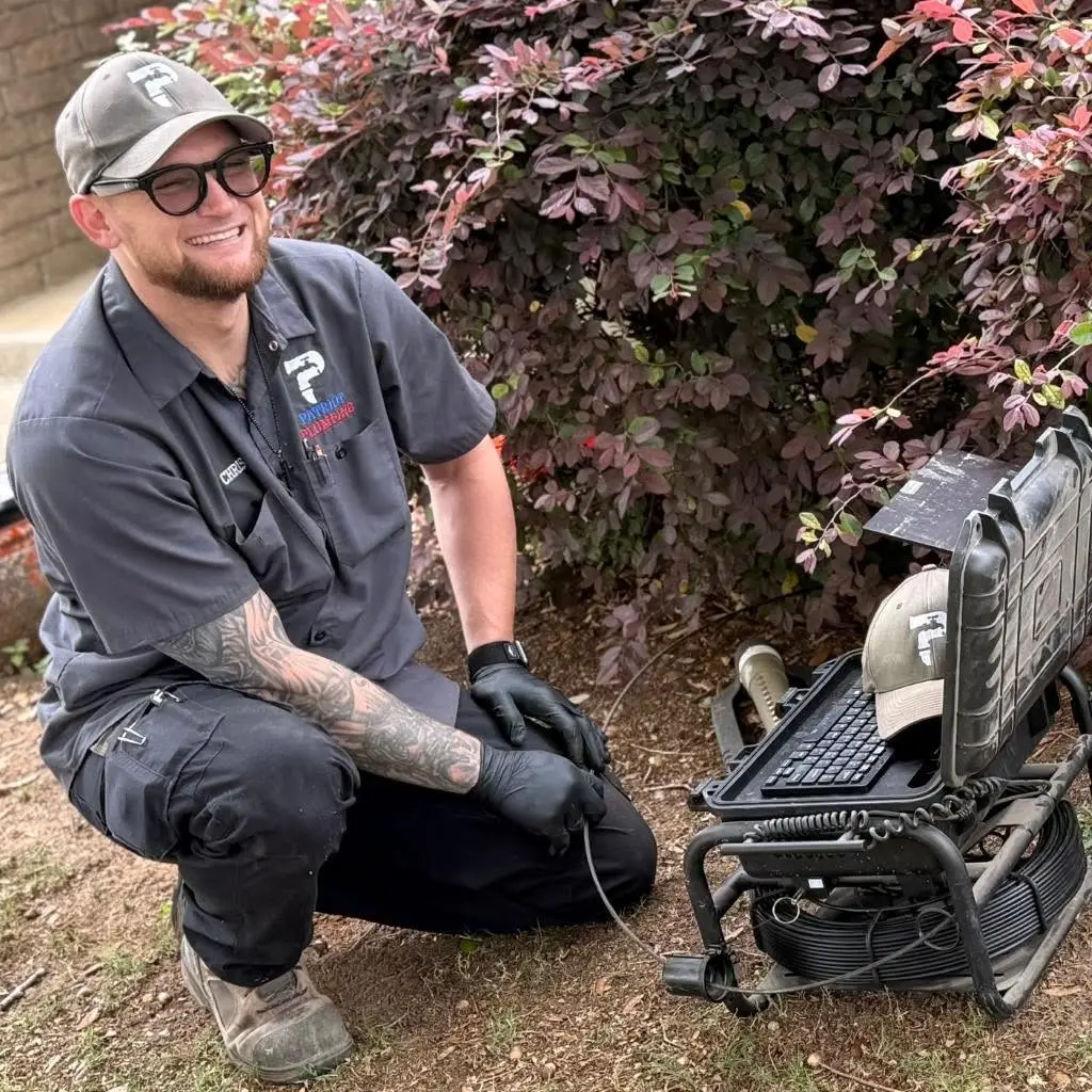 Patriot Plumbing technician in branded uniform crouching next to a portable sewer inspection system in San Antonio, TX