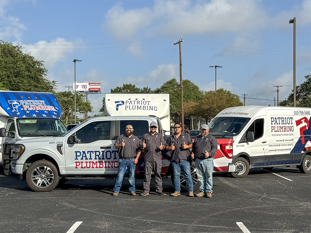 Team of four licensed Patriot Plumbing plumbers in San Antonio, Texas standing in front of branded service trucks and vans